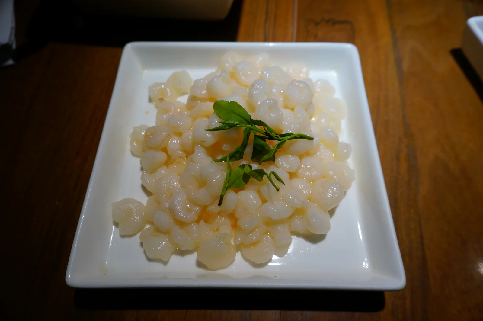 Longjing prawns on a white square plate on a wooden table, with green leaves in the centre.