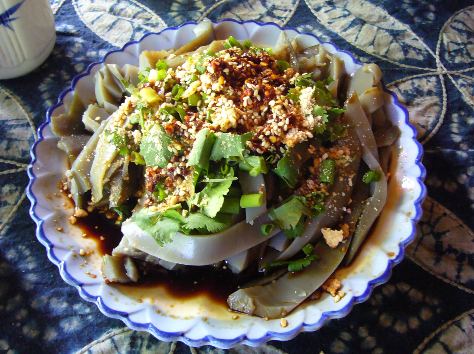 Grey-brown chickpea jelly slices with red dressing, sesame and chopped greens on a blue-rimmed plate.