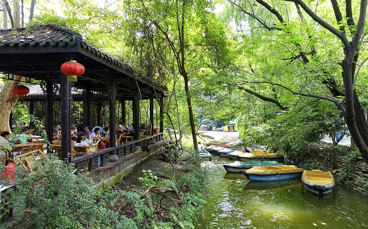 A tiled-roof teahouse and bamboo chairs beside a wooded channel with small boats in Chengdu’s People’s Park.